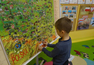 Chłopiec stoi pod mapą Polski, przyczepia napis Tatry.